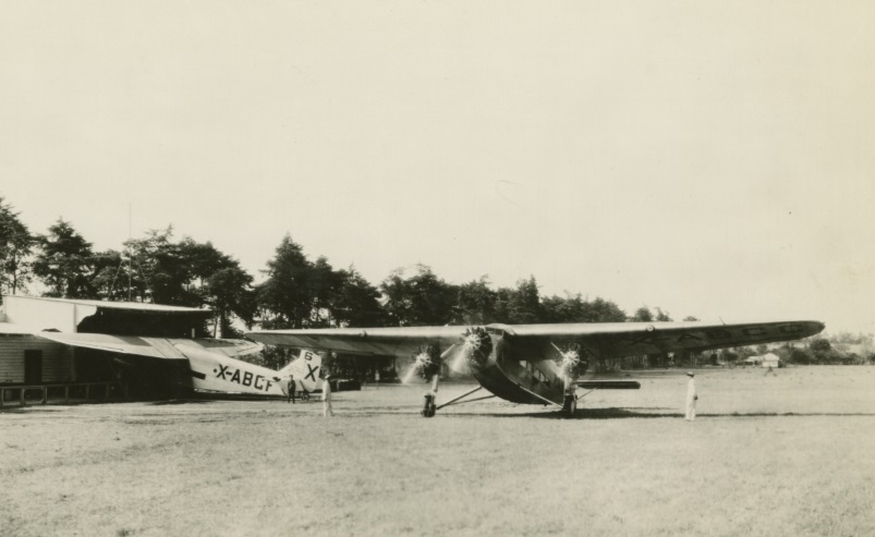 Two planes and several people in open field near low building