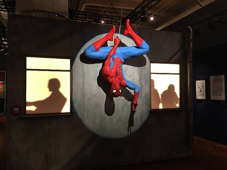 Mannequin in blue and red unitard hanging upside down in spotlight with silhouettes of people in windows on either side