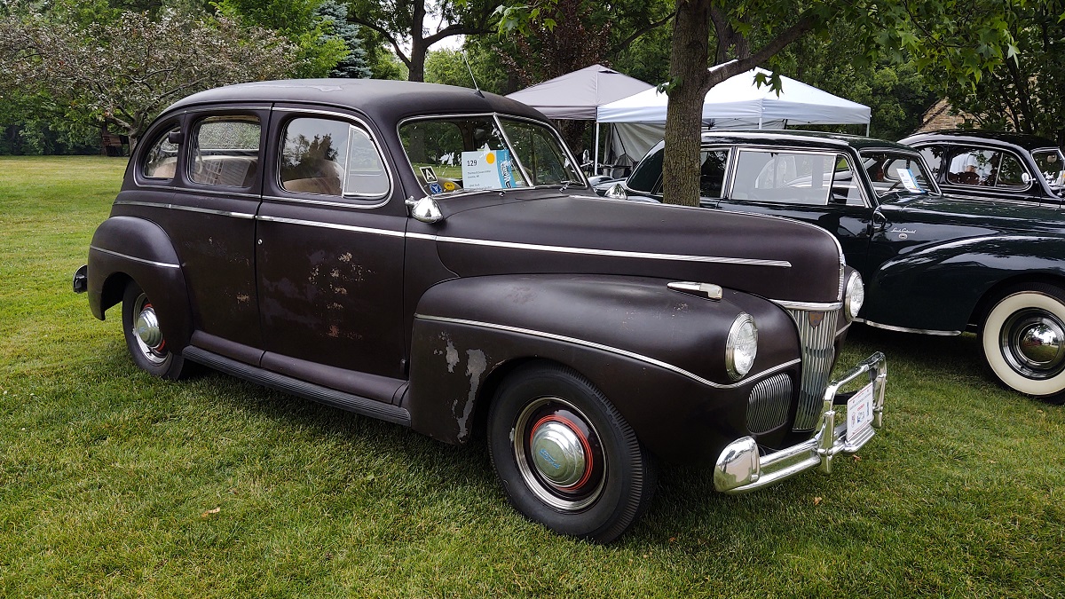 1941 Ford Super Deluxe Fordor, unrestored Long dark car with some scuffs in paint, sitting on lawn with other cars and tents nearby