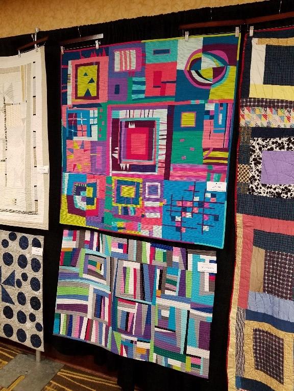 Brightly colored quilts hanging on a black backboard