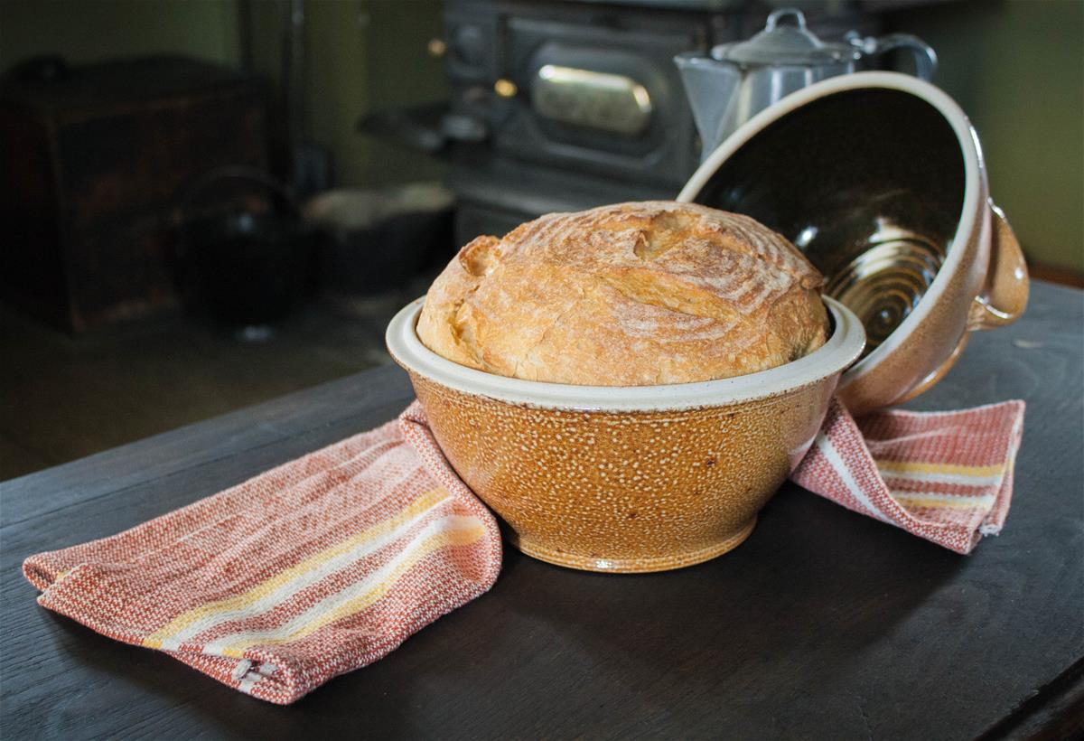 Sallie Lunn Bread in a Stoneware Bread Cloche Bread in a mustard-colored stoneware bowl with lid and red-and-white dishtowel nearby