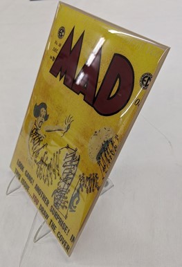 Plate stand propping up a covered and boarded comic book Yellow MAD comic book covered in plastic and on stand