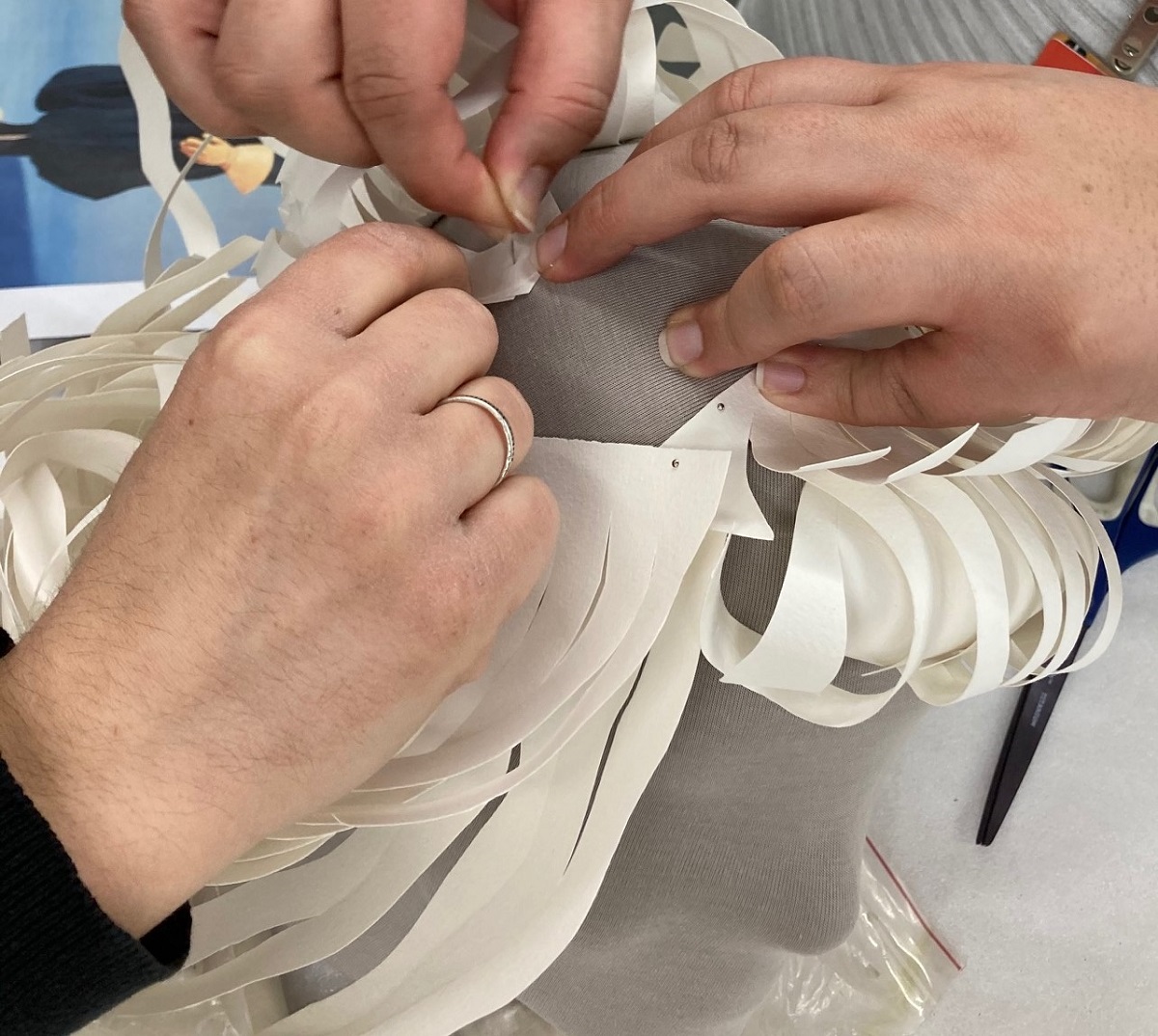 Pinning the paper wig to the mannequin head Three hands pinning curled white paper to a gray mannequin head