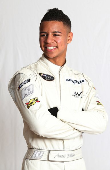 Smiling African American man with arms crossed, wearing white jumpsuit with a number of patches and logos 