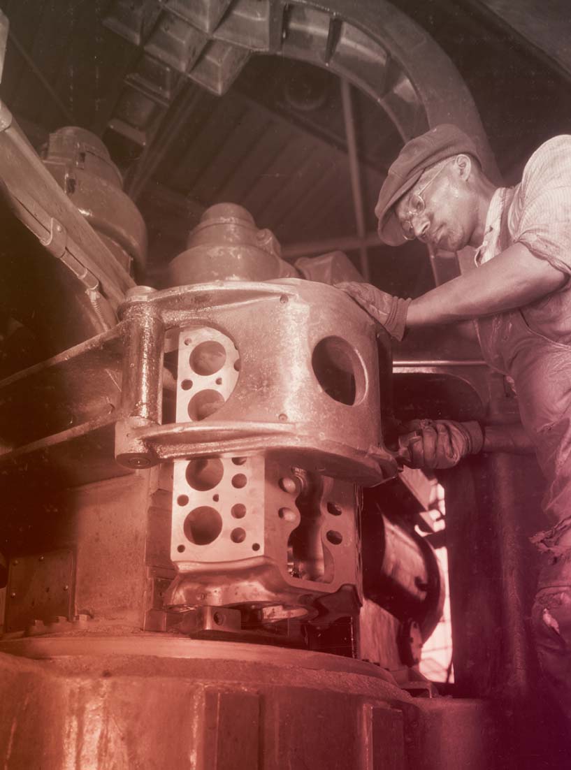 Man in work clothing and cap works at large piece of equipment
