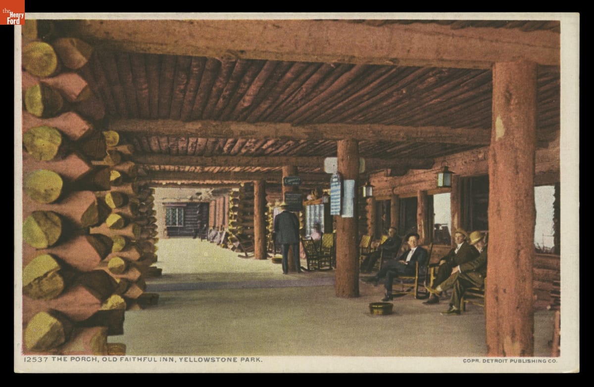 Postcard of large covered porch created from logs; people sit in rocking chairs beneath it