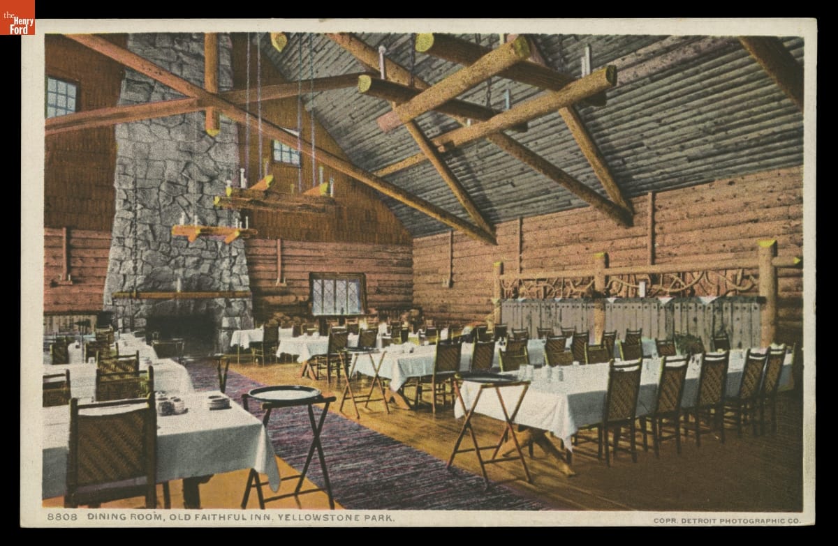 High-ceilinged rustic dining room with large wooden beams and tall fireplace containing long tables covered with white tablecloths
