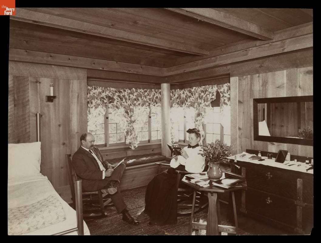 Man and woman sit reading in rocking chairs in a rustic bedroom with wooden walls