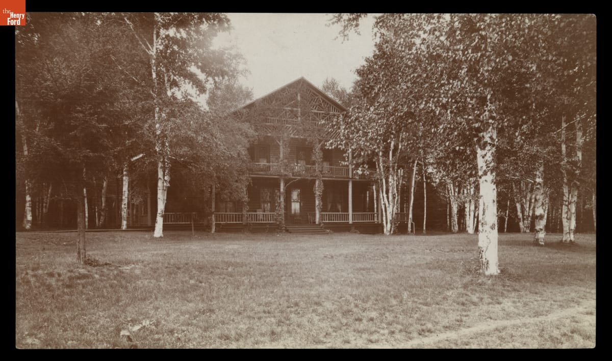 Black-and-white photo of two-story wooden building among trees
