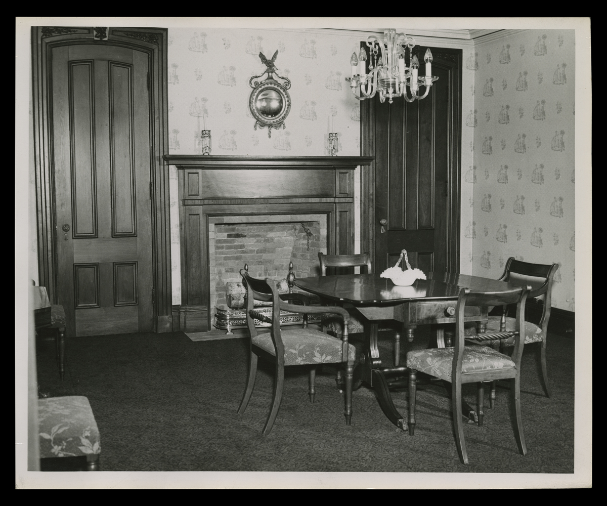 Dining Room in Noah Webster Home, Greenfield Village, 1947 Room with table and four chairs, as well as fireplace with doors on either side,