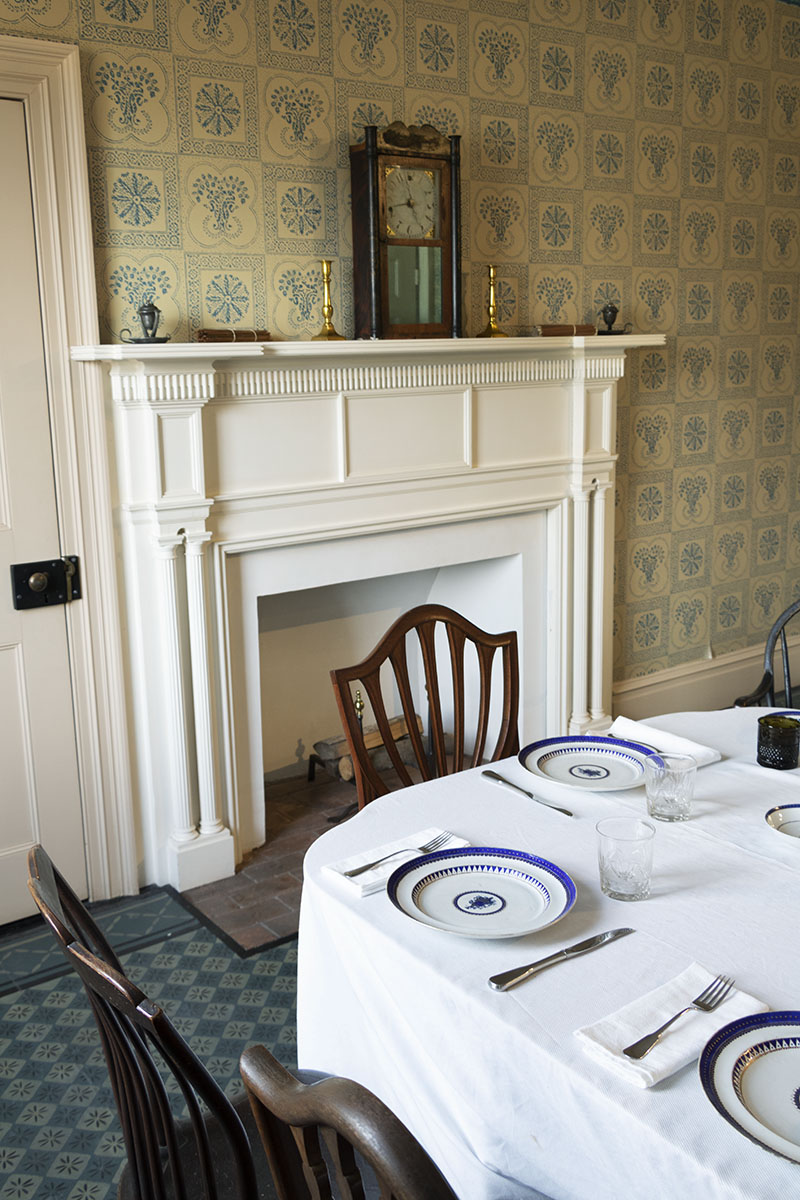 Noah Webster Home / mantel Corner of set table with chairs; fireplace with mantel behind and patterned wallpaper on walls