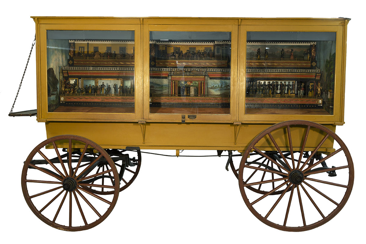 "The Busy World" Automaton Wagon, 1847 Yellow wagon with glass windows on side, behind which are small dioramas