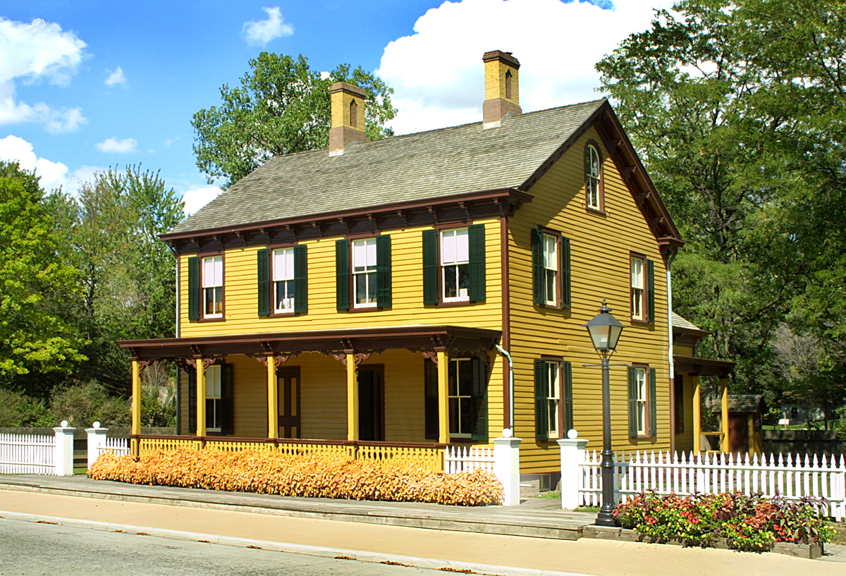 Two-story yellow wooden building with white picket fence in front