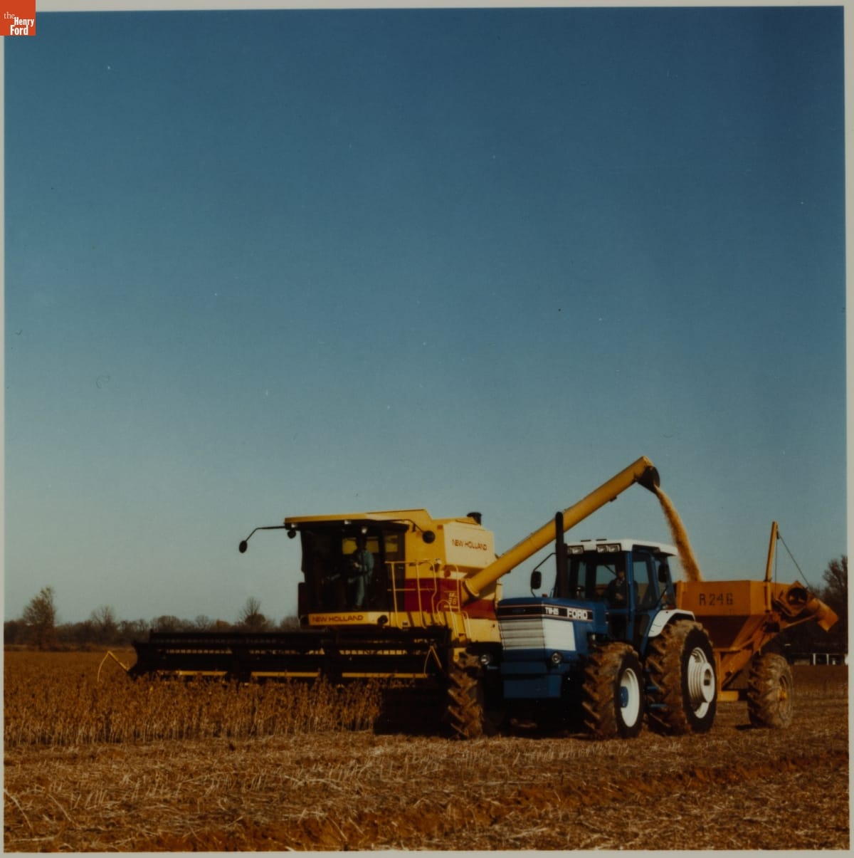 Ford New Holland Agricultural Equipment, 1985 Large blue and yellow piece of agricultural equipment harvesting crops in a field