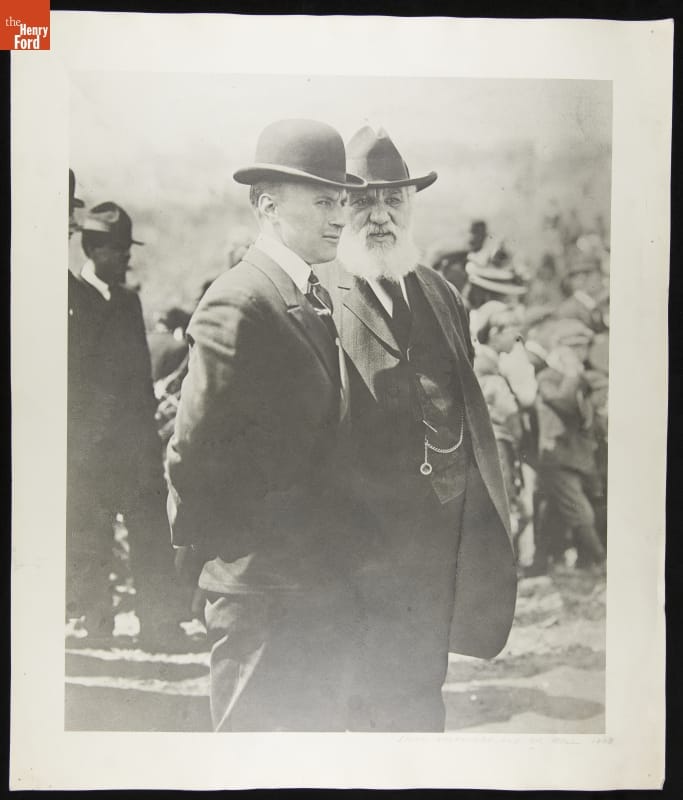 Lieutenant Thomas Selfridge and Dr. Alexander Graham Bell, 1908 Black-and-white photo of two men in suits and hats talking to each other among a crowd