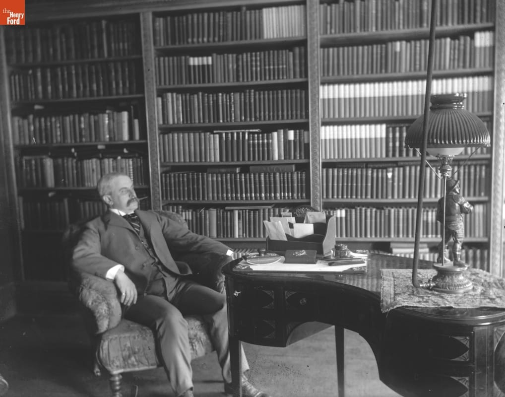 Library (W. J. Carr), 1890-1915 Photo taken by Jenny Young Chandler of a man sitting in an armchair next to a case of books in a library