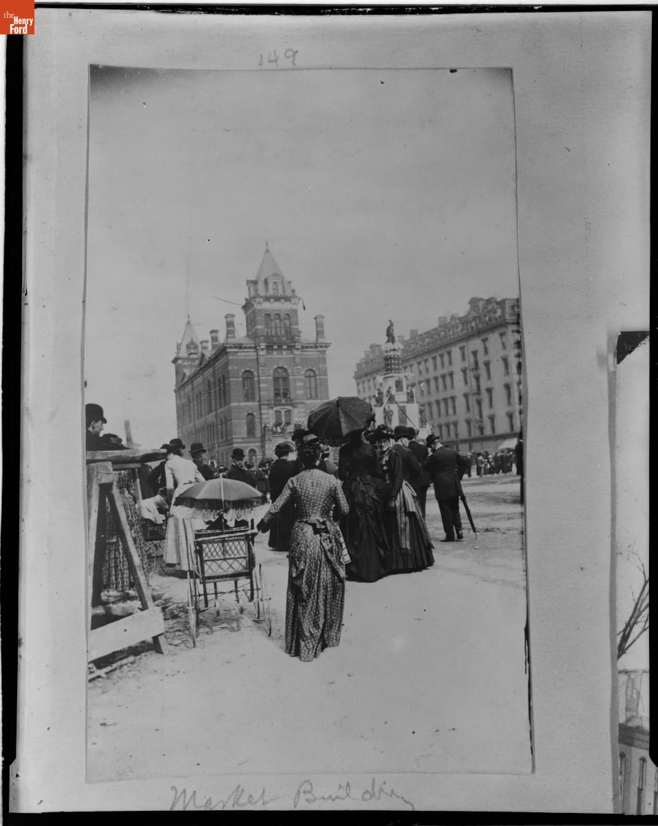 Small crowd of people, one with a baby carriage, on a street