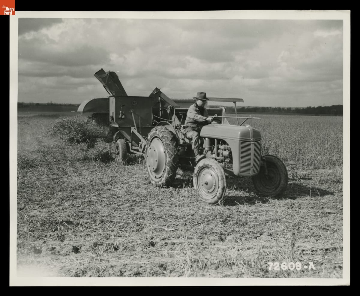 Ford-Ferguson Model 9N Tractor Pulling a Combine, Macon, Michigan, November 1939 Black-and-white photo of a person riding a tractor through a field, pulling agricultural equipment containing crops behind it