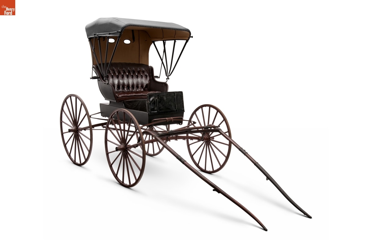 Small square buggy with four large wooden wheels and cushioned seat covered with a canopy